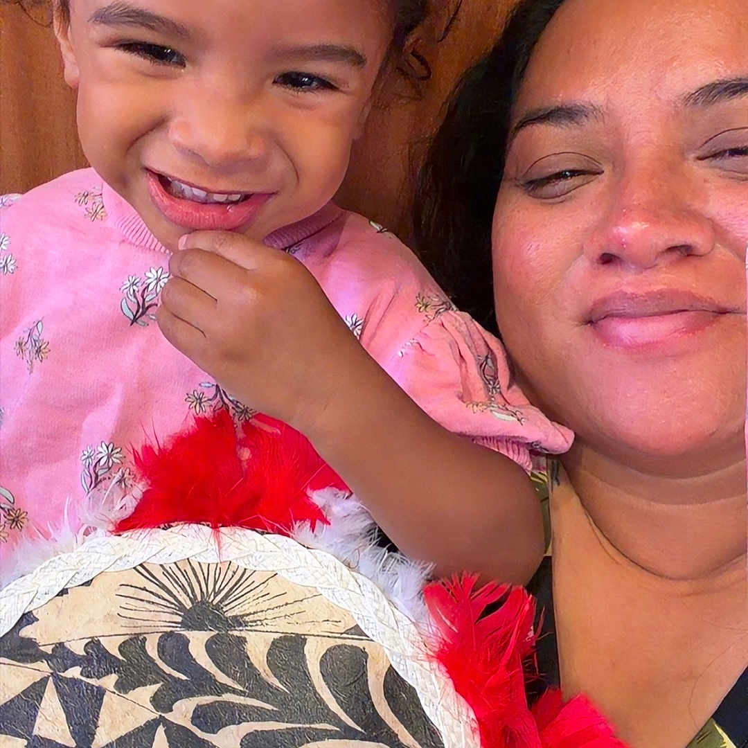 Seilose Brianna is registered to the contest to win money with this photo: child, toddler, woman, smile, face, pink_clothing, decorative_item, feathers, geometric_pattern, wooden_background, portrait, happy, family, indoor, person, cute, holding, closeup, people, casual