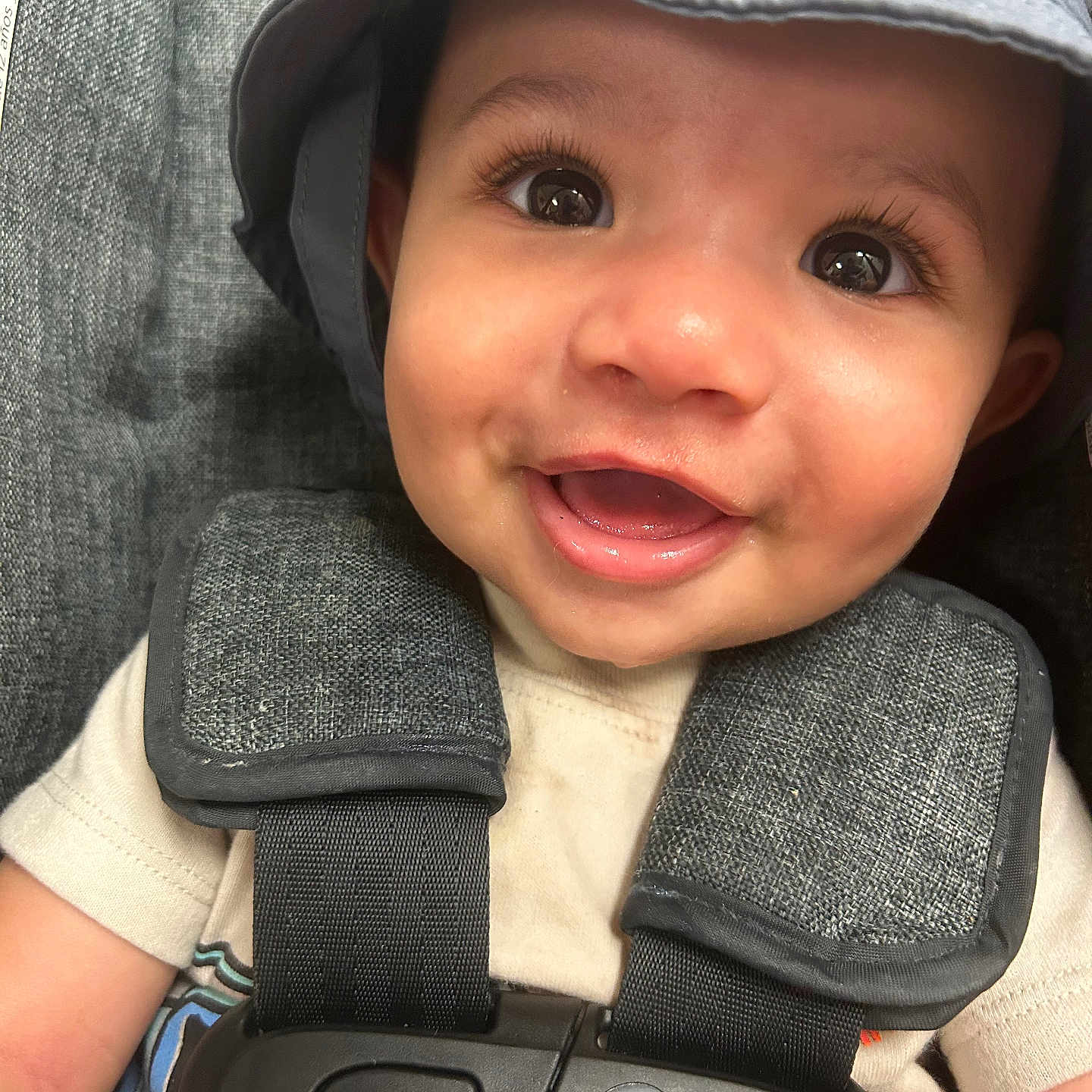 Juju is registered to the contest to win money with this photo: apparel, baby, car_seat, child, close_up, cute, expression, face, happy, hat, headwear, indoors, infant, person, portrait, safety, seat, seatbelt, smiling, young_child