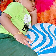 Arish is registered to the contest to win money with this photo: bed, bedding, bracelet, child, closed_eyes, colorful, comfortable, floral_pillow, green_pants, green_shirt, home, indoors, nap, peaceful, pillow, portrait, resting, side_profile, sleeping, striped_blanket