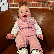 Liam is registered to the contest to win money with this photo: baby, brick_wall, brown_leather, cozy, feet, hair_tuft, hands, happy, indoor, infant, laughing, leather_chair, long_sleeves, nike, pink_outfit, polka_dot, portrait, smiling, sneakers, vest
