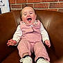 baby, brick_wall, brown_leather, cozy, feet, hair_tuft, hands, happy, indoor, infant, laughing, leather_chair, long_sleeves, nike, pink_outfit, polka_dot, portrait, smiling, sneakers, vest