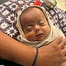 Sarah joined the competition — help win amazing prizes! newborn, baby, sleeping, infant, portrait, face, eyes_closed, swaddled, blanket, cozy, indoor, cuddling, adult_arms, medical_tube, nasal_tube, hospital_style, warm_lighting, floral_pattern, peaceful, family