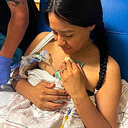 Sarah is registered to the contest to win money with this photo: newborn, baby, mother, hospital, birth, postpartum, swaddled_baby, infant, parent, caregiver, medical_equipment, iv_line, hospital_bed, blue_chair, blanket, hands, braid, portrait, family, indoors