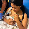 newborn, baby, mother, hospital, birth, postpartum, swaddled_baby, infant, parent, caregiver, medical_equipment, iv_line, hospital_bed, blue_chair, blanket, hands, braid, portrait, family, indoors