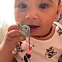 toddler, child, pacifier, beaded_necklace, cartoon_clothing, minnie_mouse, close_up, cute, baby, indoor, person, hand, face, expression, soft_lighting, casual_wear, curious, infant, portrait, holding