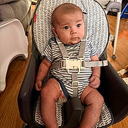 Gabriel joined the competition — help win amazing prizes! baby, infant, child, baby_seat, striped_clothing, safety_harness, indoor, wooden_floor, furniture, high_chair, seat, person, cute, young_child, home, living_room, expression, face, small_hands, legs