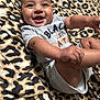 baby, smiling, infant, onesie, grey_clothing, leopard_print, blanket, happy, cute, child, skin, face, lying_down, small_hands, small_feet, indoors, infant_clothing, cheerful, person, portrait