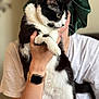 affection, black_and_white_cat, blurred_background, cat, close_up, curious, domestic_animal, expression, face, feline, hand, headwrap, holding, indoor, indoor_lighting, person, pet, portrait, watch, white_shirt