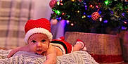 Lyle joined the competition — help win amazing prizes! baby, infant, christmas_tree, holiday, festive, red_hat, blanket, ornaments, lights, indoors, cute, holiday_season, decorations, christmas, smiling, face, soft_texture, seasonal, toddler, christmas_outfit