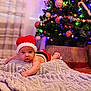 baby, infant, christmas_tree, holiday, festive, red_hat, blanket, ornaments, lights, indoors, cute, holiday_season, decorations, christmas, smiling, face, soft_texture, seasonal, toddler, christmas_outfit