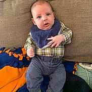 Lyle joined the competition — help win amazing prizes! baby, infant, plaid_shirt, blue_eyes, green_socks, navy_pants, bib, couch, blanket, indoor, child, person, cute, young, seated, cozy, comfortable, soft_fabric, expression, casual_clothing