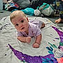 baby, child, infant, blanket, purple, crescent_moon, floral, floor, indoors, clothing, onesie, curious, face, expression, hand, foot, person, background, bag, pile_of_clothes