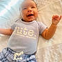 baby, infant, smiling, happy, cute, blue_shirt, plaid_shorts, lying_down, blanket, soft_texture, child, young, clothing, portrait, expression, indoors, skin, face, hand, joy