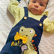 Zayne joined the competition — help win amazing prizes! baby, infant, child, dinosaur, clothing, onesie, yellow_bow, curly_hair, blanket, soft_texture, cute, portrait, indoors, laying_down, expression, face, wide_eyes, button, pattern, fabric