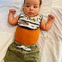 Zayne joined the competition — help win amazing prizes! baby, infant, child, bib, striped_bib, orange_top, green_shorts, dinosaur_print, dinosaur_patch, lying_down, blanket, curious_expression, raised_fists, soft_lighting, indoors, portrait, cute, clothing, young_child, face