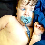 Cash is registered to the contest to win money with this photo: baby, child, pacifier, blue_eyes, close_up, infant, skin, hand, portrait, lying_down, blue_fabric, straps, cute, young, face, expression, indoors, soft_light, resting, sleepy