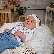 Lila participe au concours pour gagner de l'argent avec cette photo : baby, infant, headband, blue_clothing, flower_pattern, knitted_blanket, basket, wooden_furniture, decor, floral, indoor, portrait, cute, child, resting, soft_texture, cozy, homedecor, smiling, relaxed