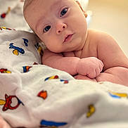 Maria is registered to the contest to win money with this photo: baby, infant, blanket, cartoon, colorful, cute, face, expression, gaze, head, indoors, lamp, lighting, looking, person, portrait, resting, skin, soft, toddler