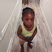 Kalani Douglas joined the competition — help win amazing prizes! toddler, child, braided_hair, barefoot, hallway, wooden_floor, white_wall, curious, standing, indoors, person, young_child, colorful_clips, casual_clothing, looking_up, small_object, feet, close_up, portrait, home