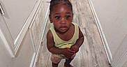 Kalani Douglas is registered to the contest to win money with this photo: adult_feet, barefoot, braided_hair, child, curious, feet, floor, hair_accessories, hallway, hands, home, indoor, person, shorts, skin, standing, toddler, wall, wooden_floor, yellow_shirt
