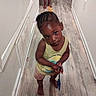 Kalani Douglas is registered to the contest to win money with this photo: toddler, child, hallway, barefoot, toy, shovel, wooden_floor, white_wall, curious, portrait, indoor, casual_clothing, shorts, tank_top, braided_hair, standing, looking_up, playtime, home, person