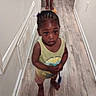 Kalani Douglas joined the competition — help win amazing prizes! toddler, child, barefoot, hallway, wood_floor, yellow_tank_top, shorts, braided_hair, indoor, person, curious, standing, expression, holding_object, adult_feet, walls, baseboard, door, flooring, lighting