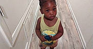 Kalani Douglas joined the competition — help win amazing prizes! child, toddler, barefoot, hallway, wooden_floor, yellow_tank_top, shorts, hair_buns, holding_object, curious, indoor, walls, vent, floor, standing, looking_up, person, young_child, casual_clothing, home