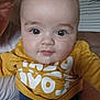 baby, child, drool, face, eyes, glasses, home, indoor, mustard_shirt, person, portrait, sitting, toddler, white_text, yellow_clothing, closeup, couch, adult, partial_face, casual