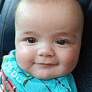 Nélyo participe au concours pour gagner de l'argent avec cette photo : baby, child, face, smile, eyes, blue_clothing, infant, cute, portrait, cheeks, head, person, sitting, patterned_background, closeup, young_child, happy, skin, indoors, casual
