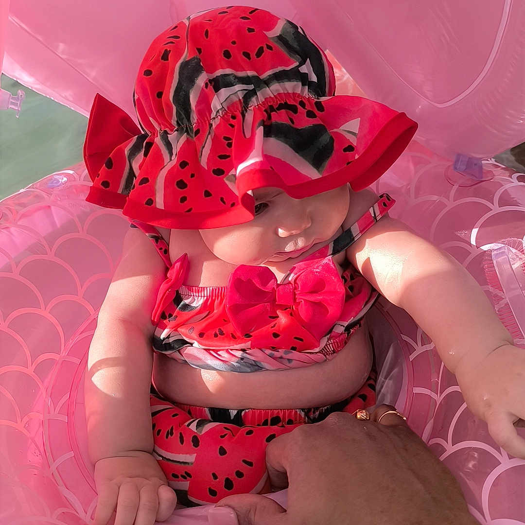 Tiyana participe au concours pour gagner de l'argent avec cette photo : adult, baby, child, chubby, cute, hand, hat, holding, inflatable_float, outdoor, pink, playful, sitting, skin, summer, sunlight, swimsuit, vacation, water, watermelon_pattern