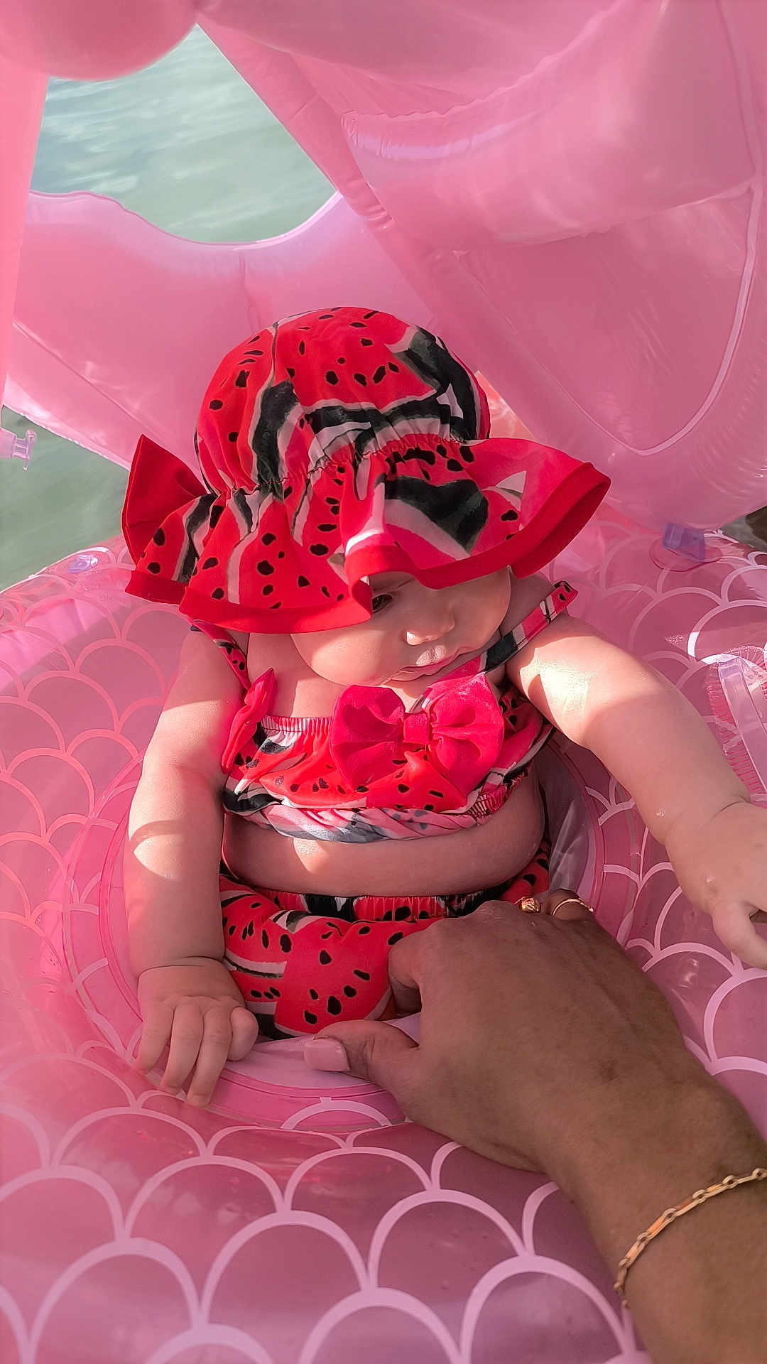 Tiyana participe au concours pour gagner de l'argent avec cette photo : baby, child, swimsuit, hat, watermelon_pattern, inflatable_float, pink, water, hand, adult, sunlight, summer, outdoor, cute, chubby, skin, sitting, holding, vacation, playful