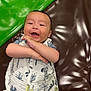 animal_print, baby, brown_surface, child, closeup, crossed_arms, cute, expression, green_cushion, happy, indoors, infant, lying_down, person, playful, portrait, skin, smiling, white_outfit, young_child