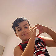 Enzo a rejoint le concours — aidez-le/la à gagner de superbes lots ! child, boy, smile, hands, heart_shape, black_shirt, red_trim, indoor, ceiling_light, white_wall, short_hair, portrait, casual_clothing, sportswear, looking_down, young_person, expression, gesture, home, chicago_bulls