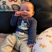 Lainey joined the competition — help win amazing prizes! baby, infant, smile, clothing, blanket, cushion, indoor, happy, face, person, sitting, soft, cute, winter, cozy, pattern, blue_shirt, gray_pants, child, comfort