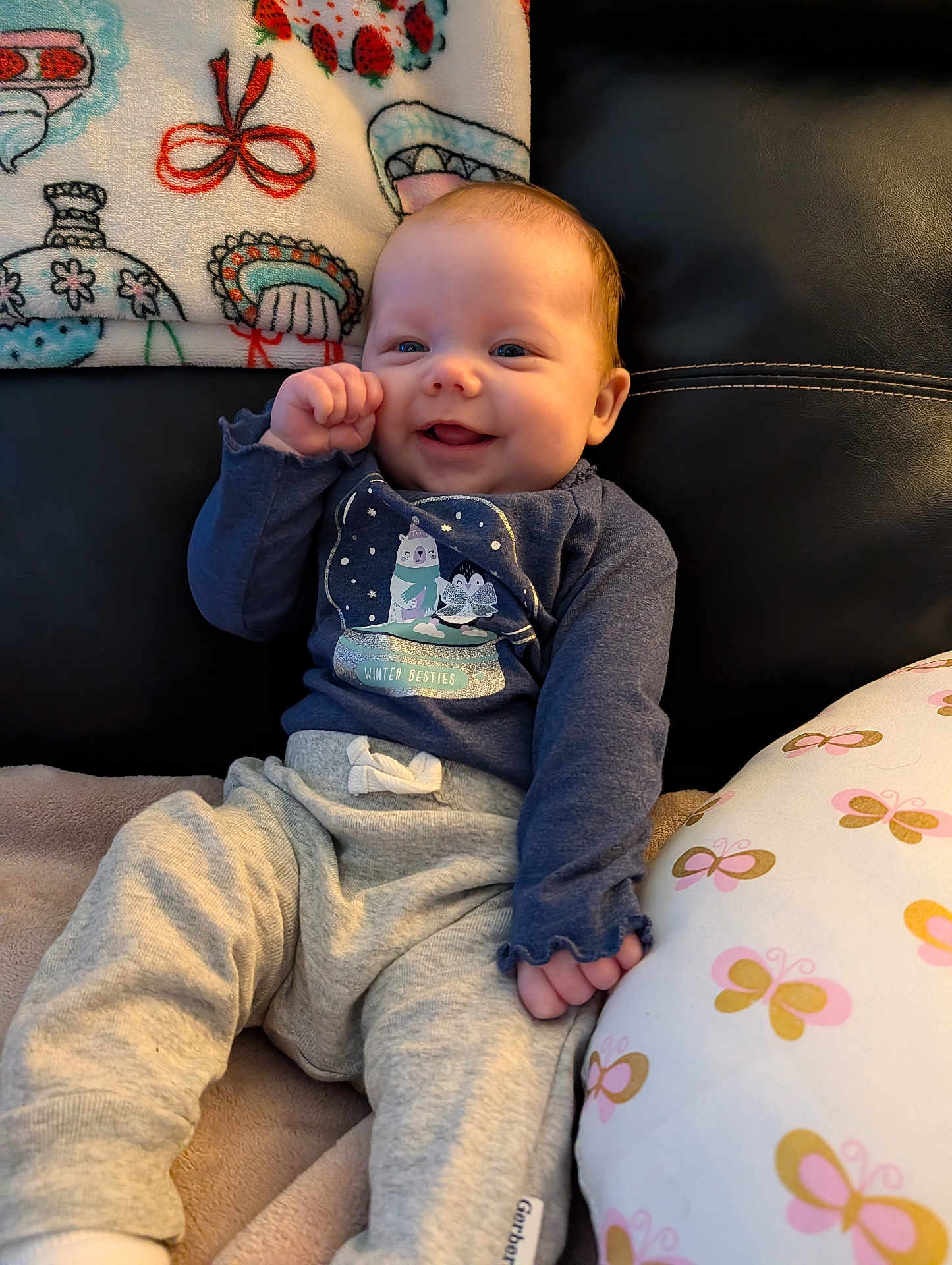 Lainey joined the competition — help win amazing prizes! baby, infant, smile, clothing, blanket, cushion, indoor, happy, face, person, sitting, soft, cute, winter, cozy, pattern, blue_shirt, gray_pants, child, comfort