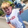 child, boy, plush_toy, white_tshirt, levi's, outdoor, daylight, blond_hair, playground, smiling, toy, casual_clothing, short_sleeves, red_trim, young, happy, person, nature, sunny, portrait