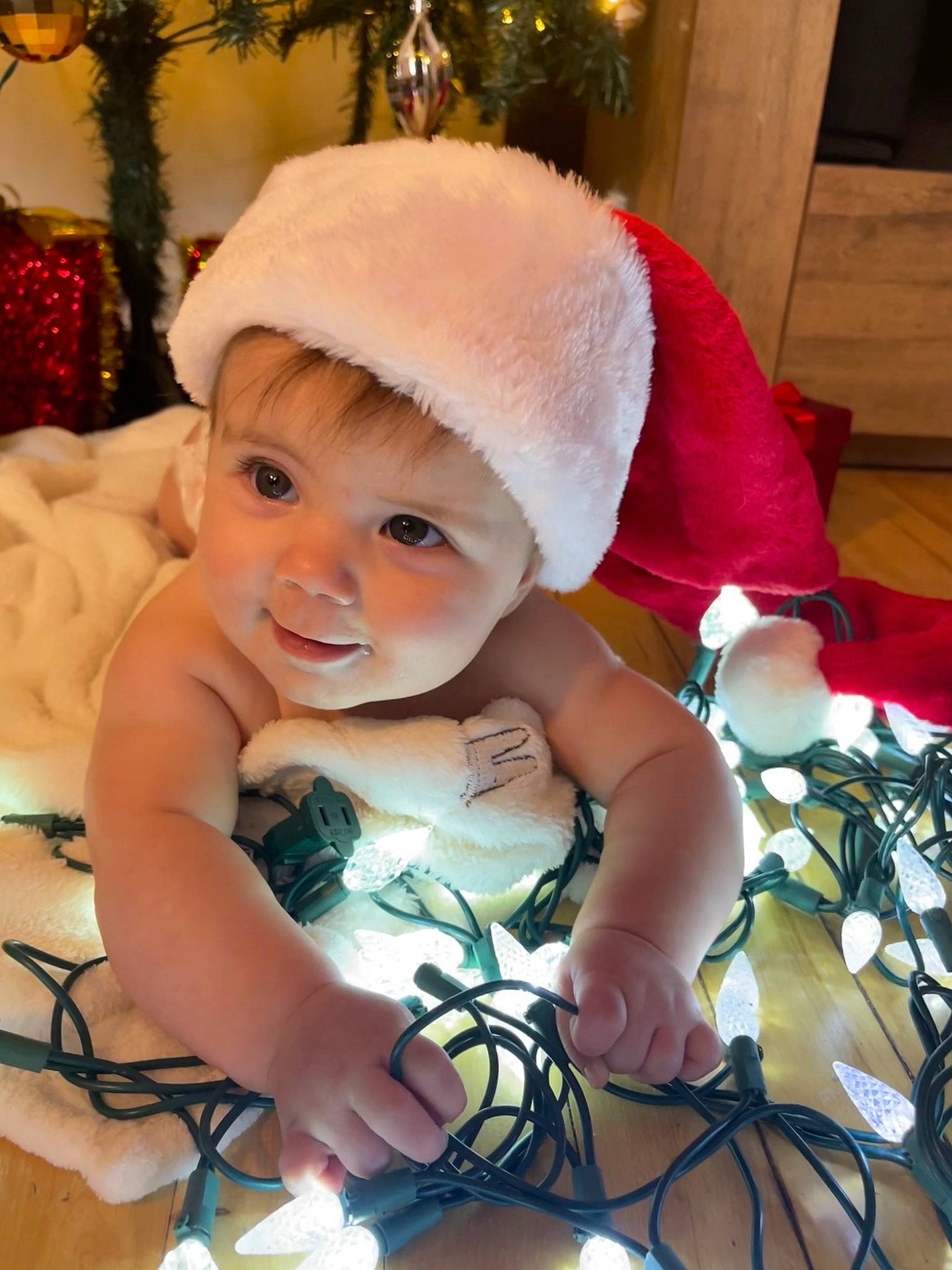 Lyannah a rejoint le concours — aidez-le/la à gagner de superbes lots ! baby, baby_toddler_clothing, christmas, christmas_eve, christmas_ornament, christmas_tree, costume_hat, event, eye, face, happy, hat, head, holiday, light, ornament, person, skin, smile, toddler