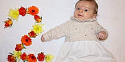 Louise a rejoint le concours — aidez-le/la à gagner de superbes lots ! baby, child, flower, number_two, orange_flower, yellow_flower, sweater, dress, lying_down, portrait, celebration, milestone, cute, infant, soft_background, floral_arrangement, skin, hand, face, eyes