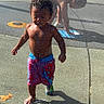 King is registered to the contest to win money with this photo: child, water, playground, splash_pad, barefoot, summer, outdoor, fun, wet, shorts, boy, playing, sunlight, shadow, water_spray, pavement, active, daytime, recreation, casual