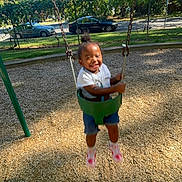 King joined the competition — help win amazing prizes! blue_shorts, casual_clothing, child, daylight, fence, fun, green_swing, happy, motion, outdoor, park, pink_shoes, playground, smiling, summer, swing, toddler, trees, white_shirt, woodchips