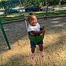 blue_shorts, casual_clothing, child, daylight, fence, fun, green_swing, happy, motion, outdoor, park, pink_shoes, playground, smiling, summer, swing, toddler, trees, white_shirt, woodchips