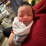 Mion joined the competition — help win amazing prizes! newborn, baby, swaddled, sleeping, hospital, blanket, person, red_sweater, indoor, infant, cradled, medical_equipment, can, furniture, closeup, face, peaceful, resting, human, care