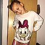 child, smiling, white_sweater, minnie_mouse, pink_leggings, indoor, wooden_panel, playful_pose, happy, person, fashion, hair_bun, closed_eyes, casual_clothing, floor, wall, home, cute, portrait, standing