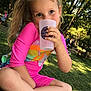 child, girl, pigtails, pink_clothing, sitting, cross_legged, drinking, cup, outdoor, park, greenery, trees, sunlight, happy, playful, summer, nature, footwear, casual, daylight