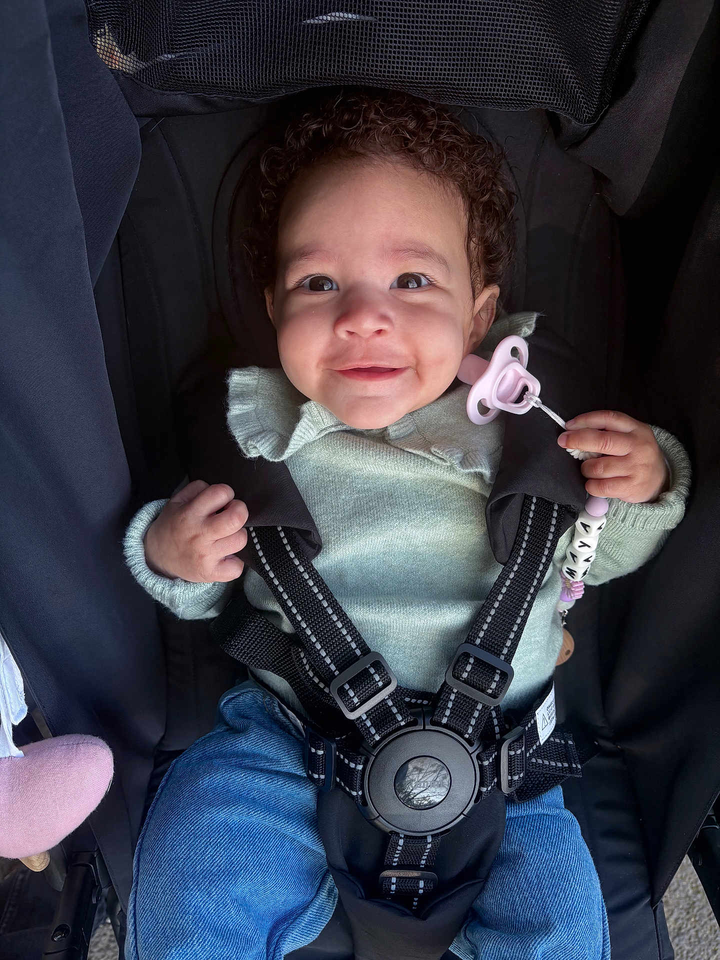 Maya participe au concours pour gagner de l'argent avec cette photo : baby, child, stroller, pacifier, curly_hair, smiling, clothing, jeans, sweater, seatbelt, happy, person, infant, cute, outdoor, hand, face, portrait, baby_accessory, child_safety