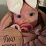 baby, infant, two_months, pacifier, bow, blanket, pink, wooden_sign, face, portrait, close_up, cute, child, newborn, soft_texture, indoors, wrapped, expression, young, adorable