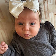 Skarlett is registered to the contest to win money with this photo: baby, infant, child, face, headband, bow, clothing, blanket, expression, cute, wide_eyes, pout, skin, hand, lying_down, indoor, portrait, soft, warm, cozy