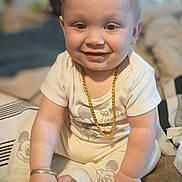 Anthony is registered to the contest to win money with this photo: baby, child, smiling, jewelry, gold_chain, bracelet, mickey_mouse, pajamas, sitting, bed, indoor, cute, happy, infant, person, face, hand, foot, clothing, toy