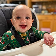 Lillian joined the competition — help win amazing prizes! baby, child, high_chair, smiling, happy, indoor, face, clothing, holiday_pajamas, green, kitchen, wooden_cabinets, infant, person, seatbelt, table, cheerful, cute, portrait, young