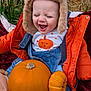 baby, child, pumpkin, orange_jacket, hat, denim_overalls, laughing, fall, autumn, cute, outdoor, plants, blanket, seasonal, happy, smiling, cozy, clothing, person, toddler